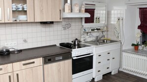 A compact kitchen with wooden cabinets, a built-in oven, a sink, and a stove. - Pension-Neuenrade (Neuenrade)