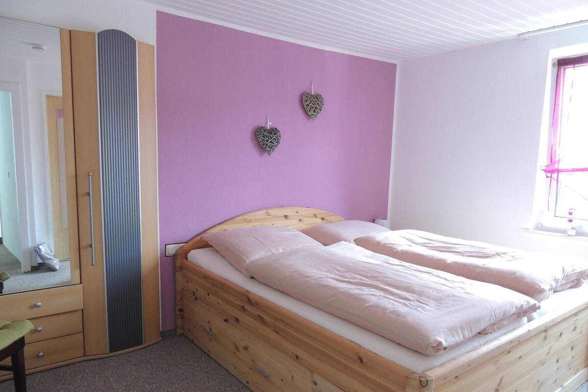 A bedroom with a wooden bed, a mirror, and a purple wall.