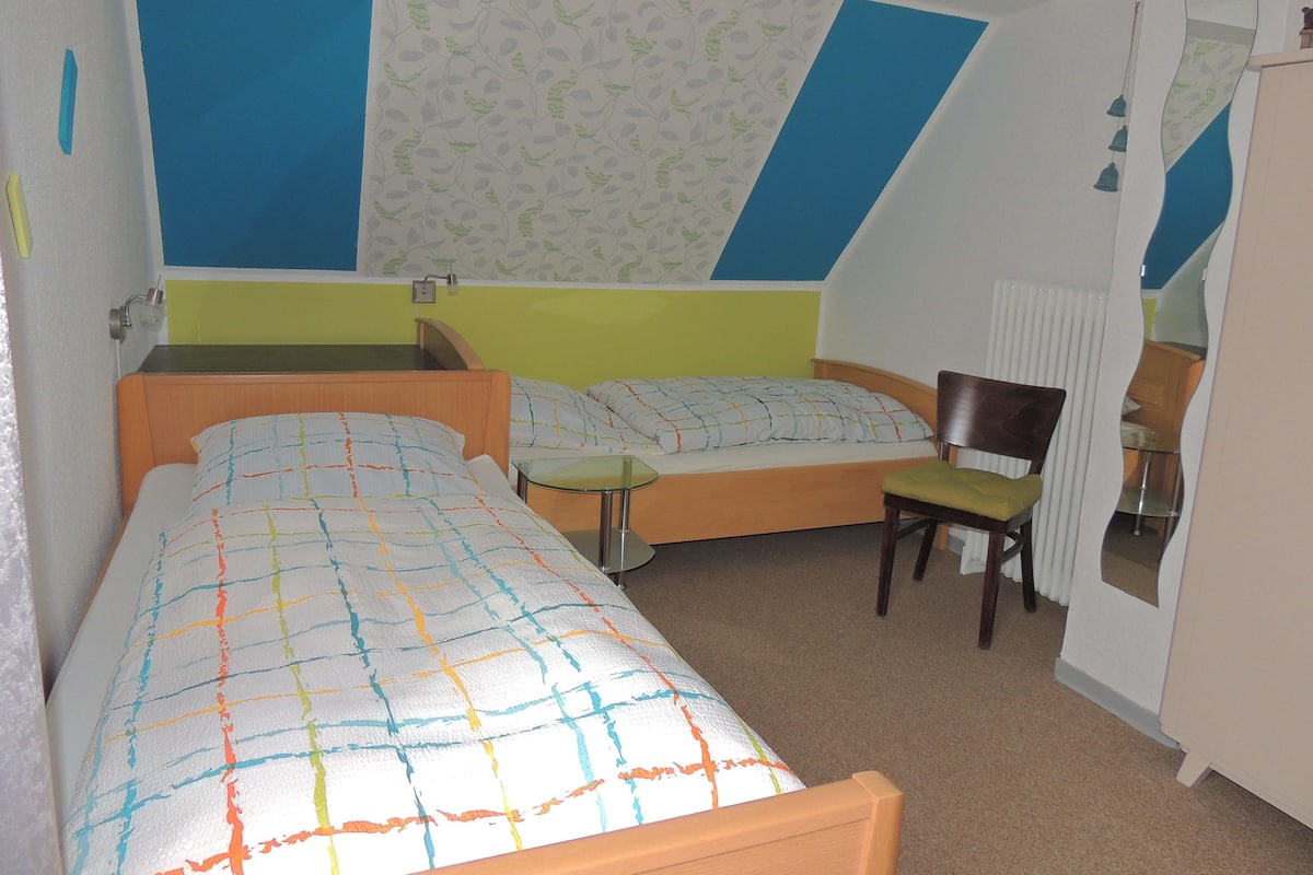 A room with two beds, a chair, a small table, and a radiator.