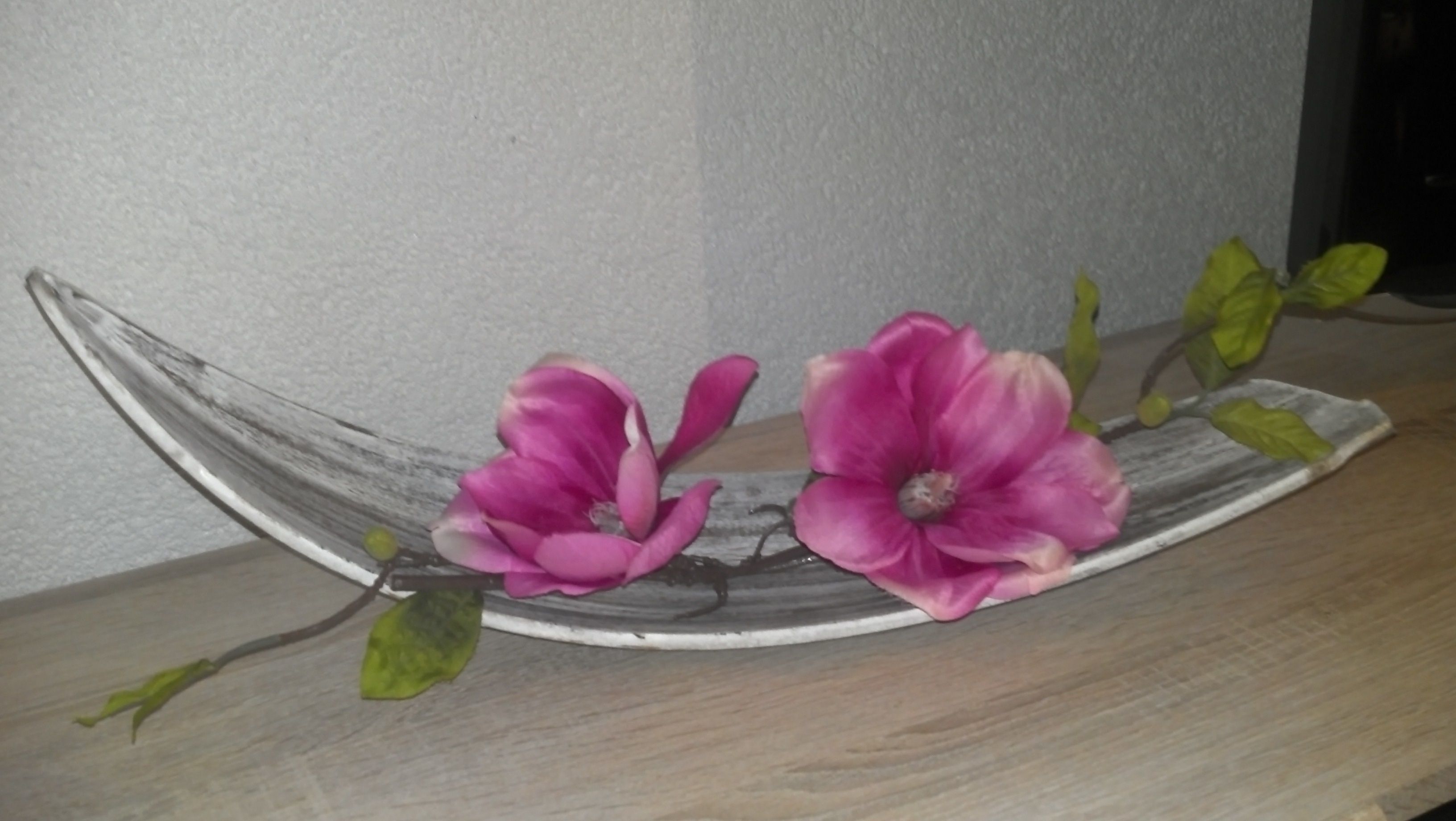 Una estantería de madera con dos flores rosas y hojas verdes.