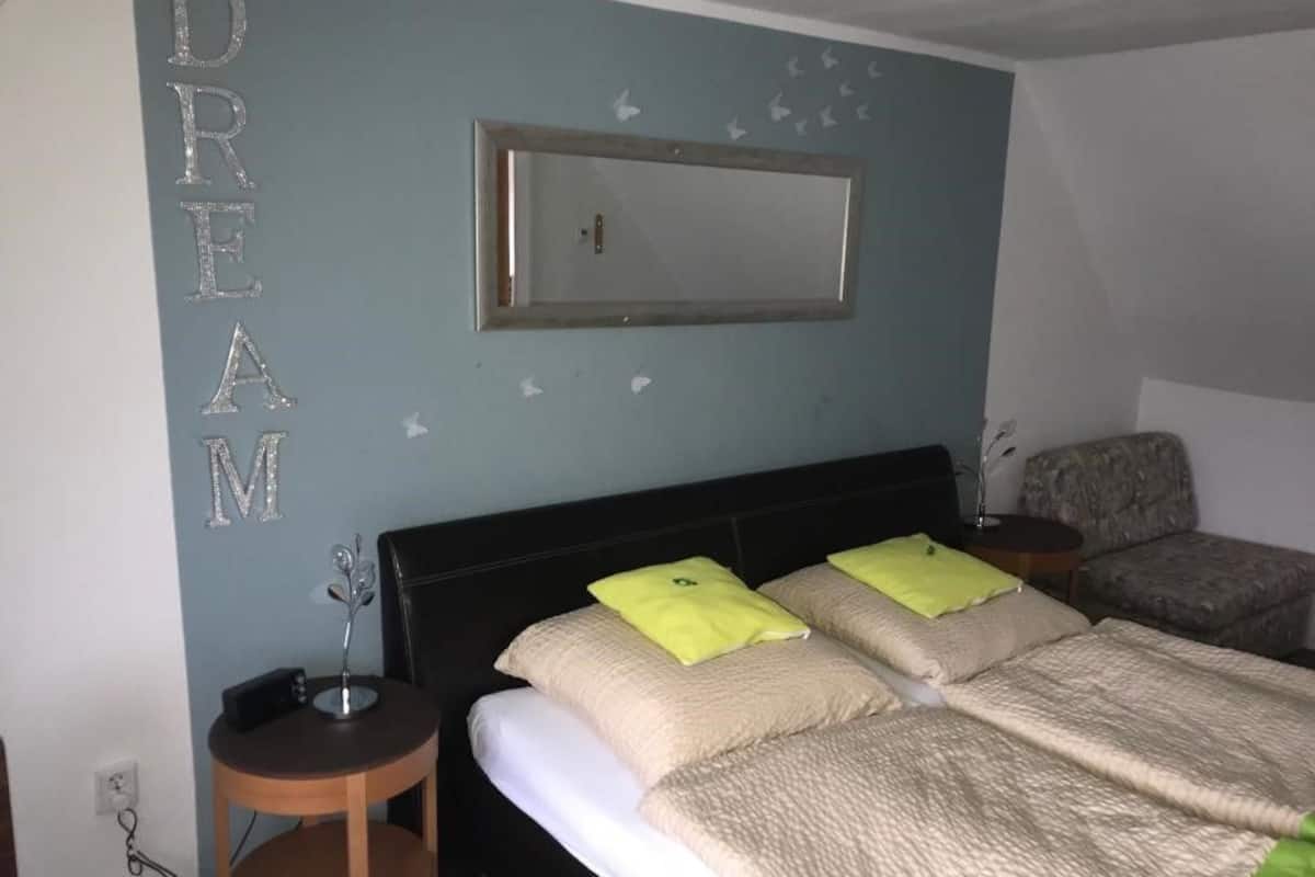 A bedroom with a bed, a nightstand, a chair, and a wall-mounted mirror.