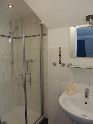 Une salle de bain avec une douche à parois de verre, un lavabo blanc et un miroir au-dessus.