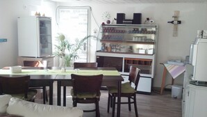 A dining area with a table, chairs, a refrigerator, a shelf with bottles, and a plant. - Pension-Neuenrade (Neuenrade)