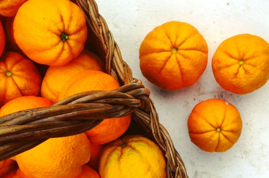 A basket of oranges with a wicker handle.