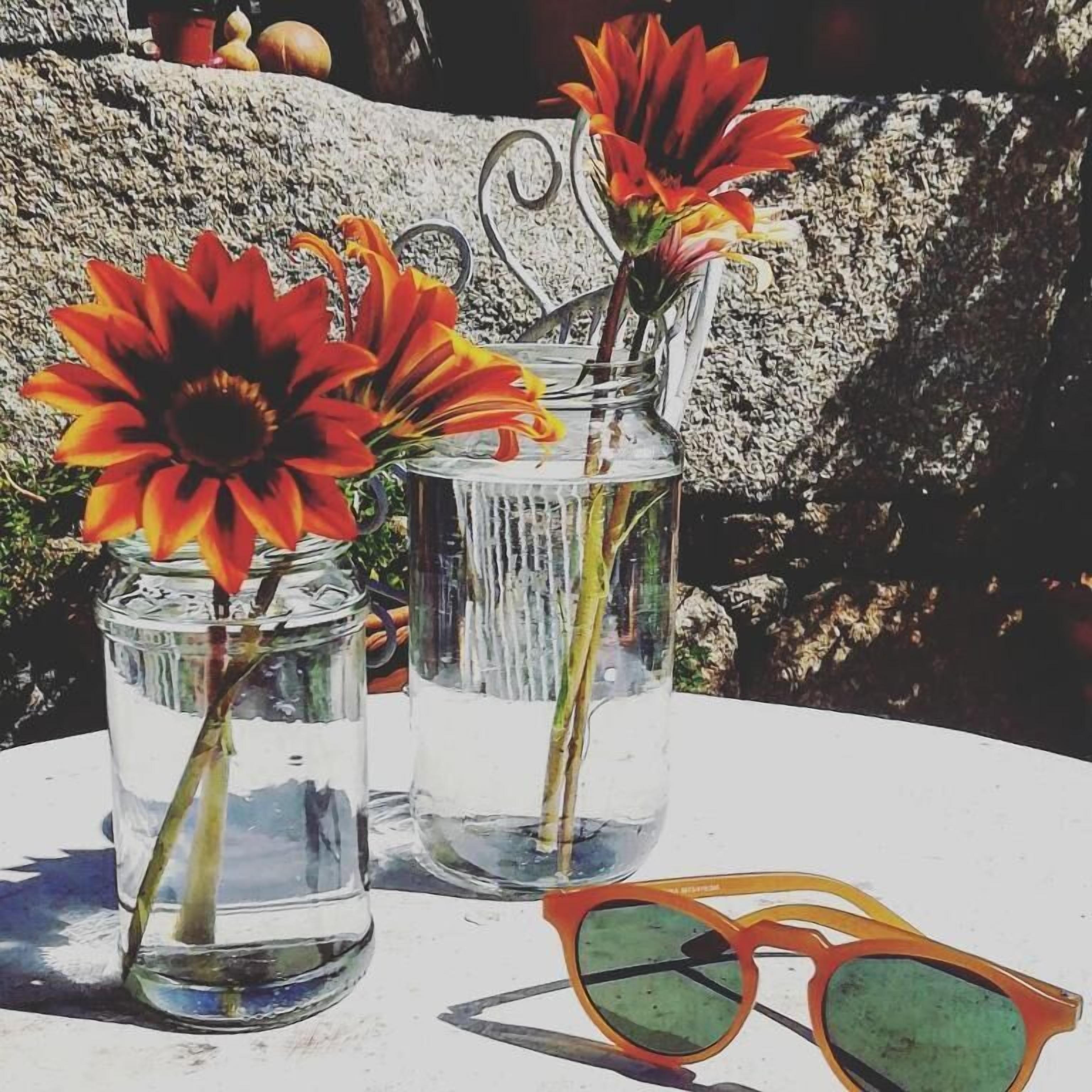Drie glazen vazen met bloemen en een zonnebril op een tafel.