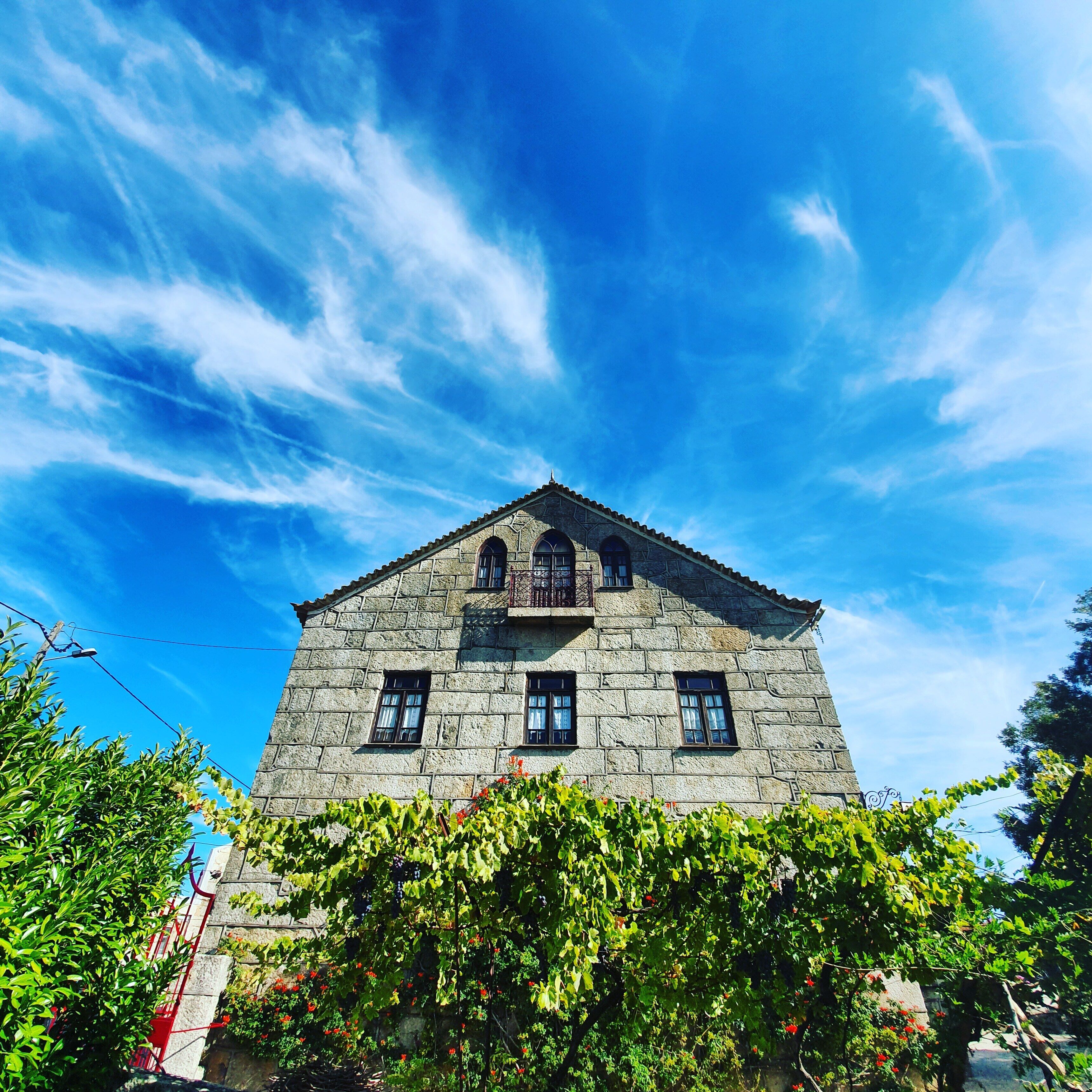 A stone building with a triangular roof and multiple windows, surrounded by greenery.