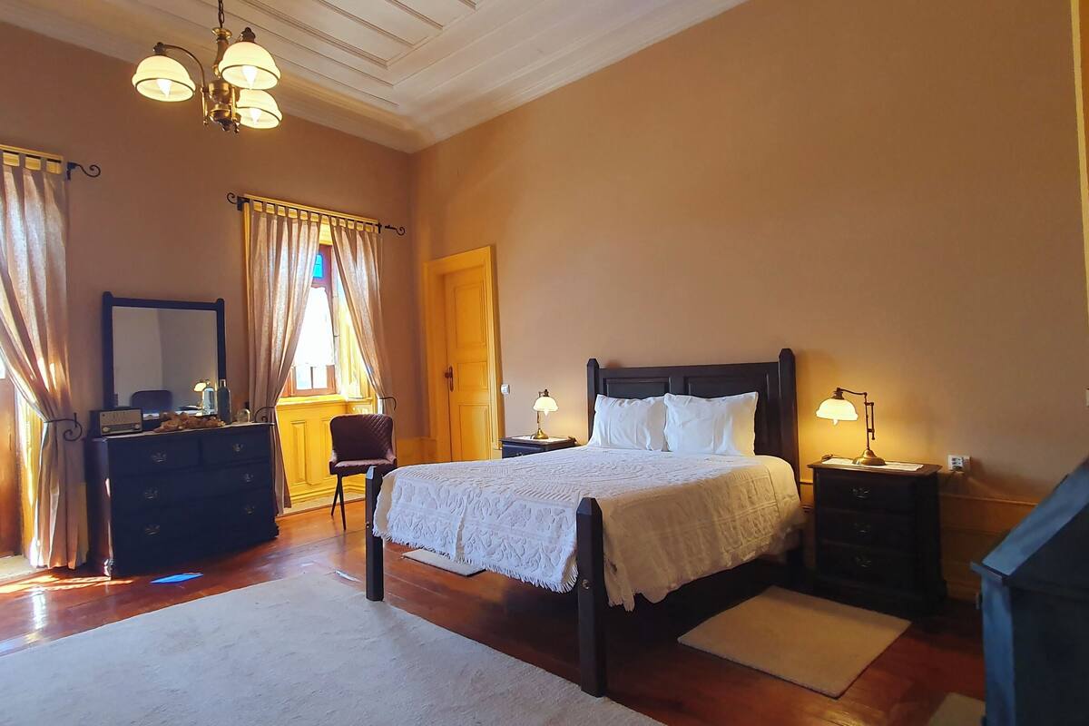 A bedroom with a wooden bed, a dresser, a chair, and a desk with lamps.