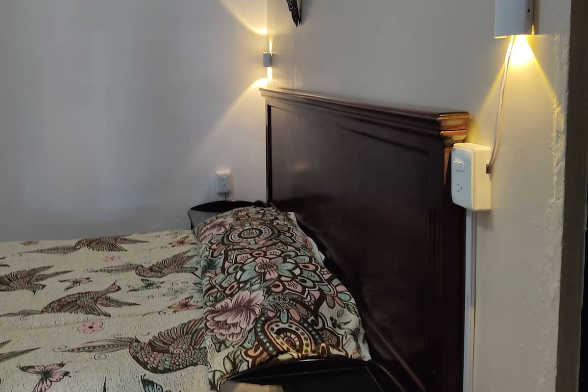 A bedroom with a bed, a bedside table, a nightstand, and wall-mounted lights.