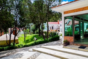 A modern building with large glass windows, a stone pathway, and a well-maintained garden with trees and a lawn. - Villas Xänthe Rotamundos (Huasca de Ocampo)
