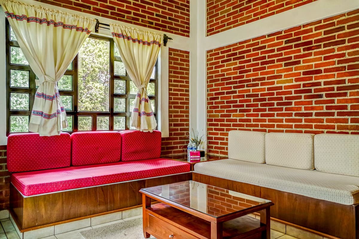 A living room with a red and white sofa, a glass coffee table, and a brick wall.