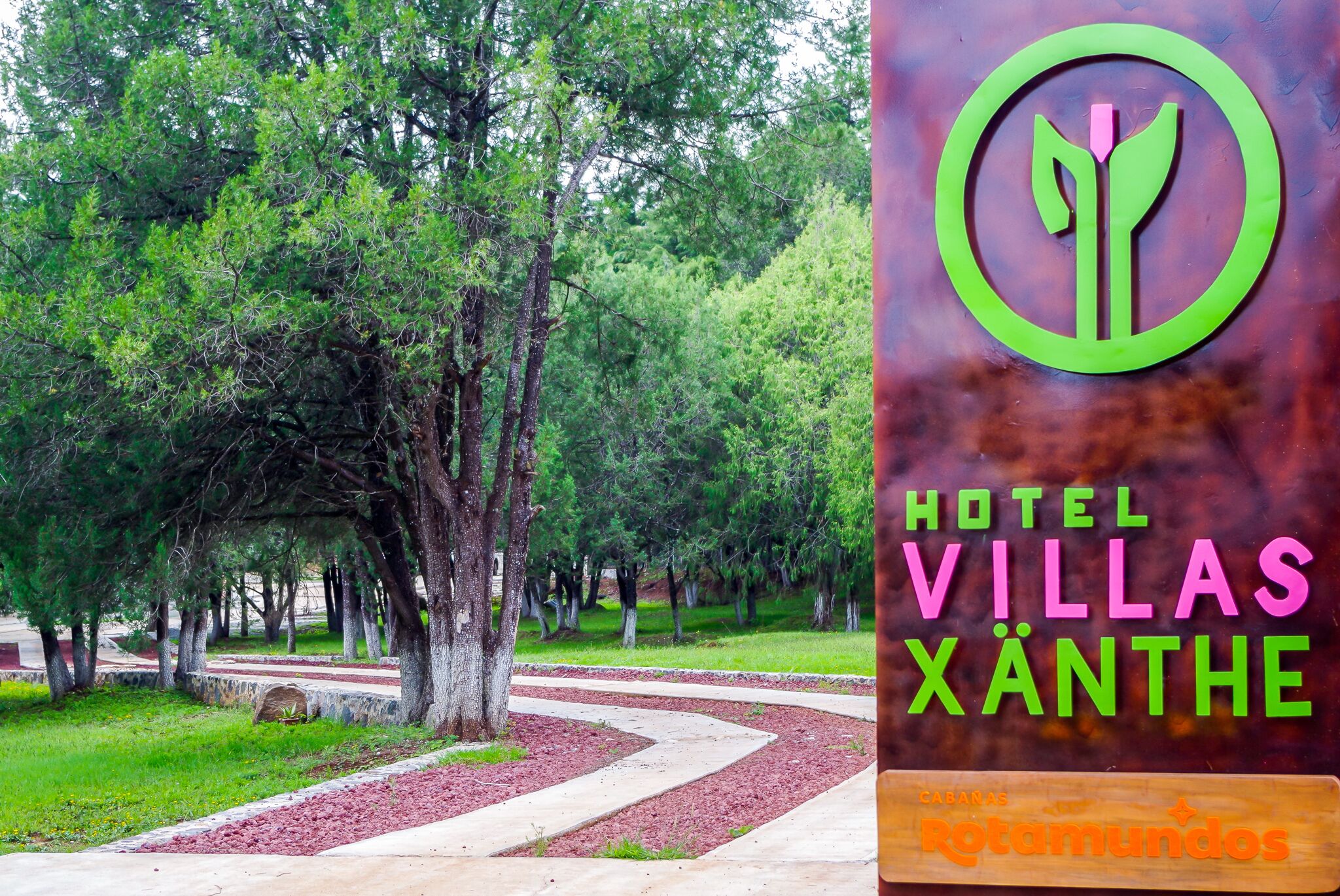 Skilt for Hotel Villas Xanthe med et logo, der viser en stiliseret plante.