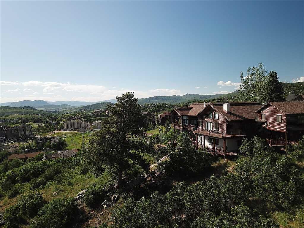 A large, multi-story house with a prominent balcony, surrounded by lush greenery and mountains in the background.