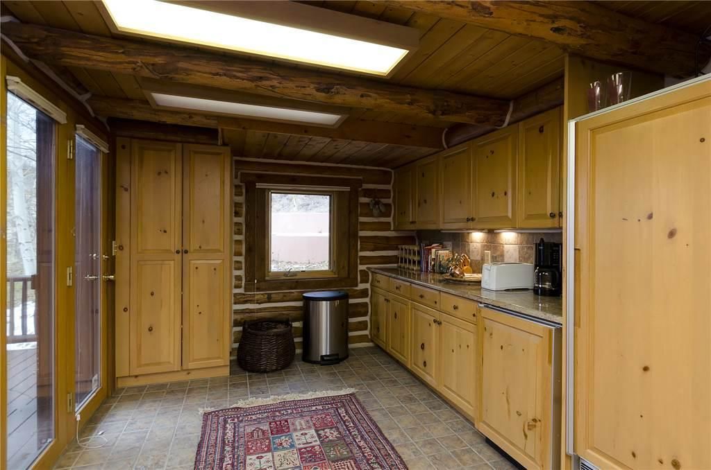 A log cabin kitchen with wooden cabinets, a window, a trash can, and a rug.