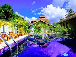 A swimming pool with a clear view of the surrounding lush greenery and a building with a red-tiled roof.