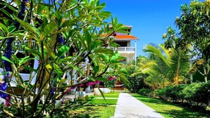 A pathway leading to a building with a balcony, surrounded by lush greenery and palm trees. - Thambili cabanas (Hikkaduwa)