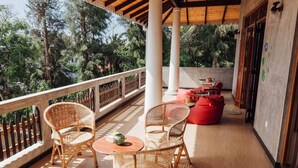 A covered outdoor seating area with wicker chairs and a small table, a red bean bag, and a wooden floor. - Thambili cabanas (Hikkaduwa)
