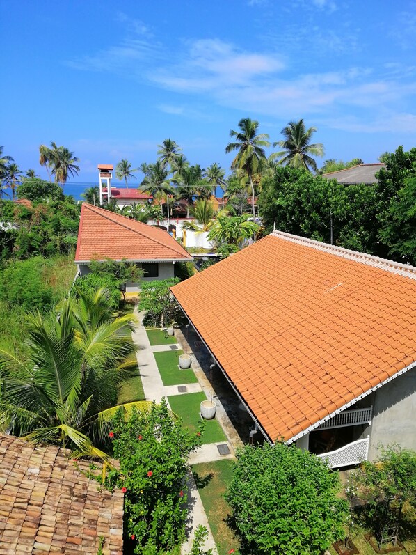 A residential area with houses featuring red-tiled roofs, surrounded by lush greenery and palm trees.