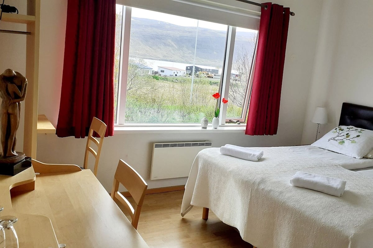 A bedroom with a bed, a chair, a table, and a window with curtains.