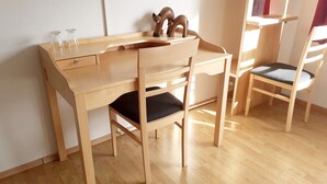 A wooden desk with a chair, a small glass vase, and a wooden fox figurine.