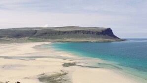 A coastal landscape with a sandy beach, clear turquoise waters, and a prominent cliff.