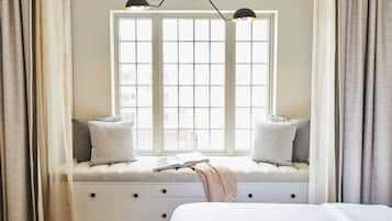 A bedroom with a large window, a bed, and a bench with pillows.