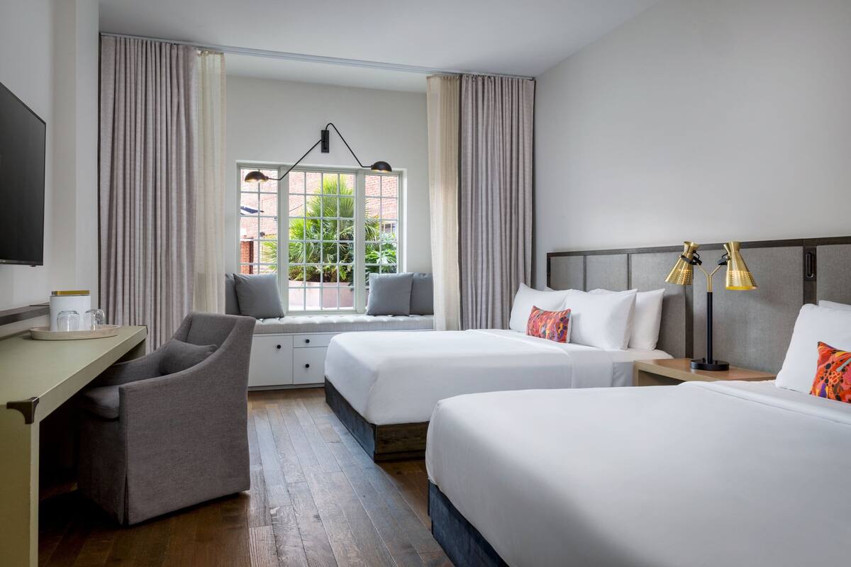 Ein Hotelzimmer mit zwei Betten, einem Schreibtisch, einem Stuhl, einem Fernseher und einem Fenster mit Vorhängen.