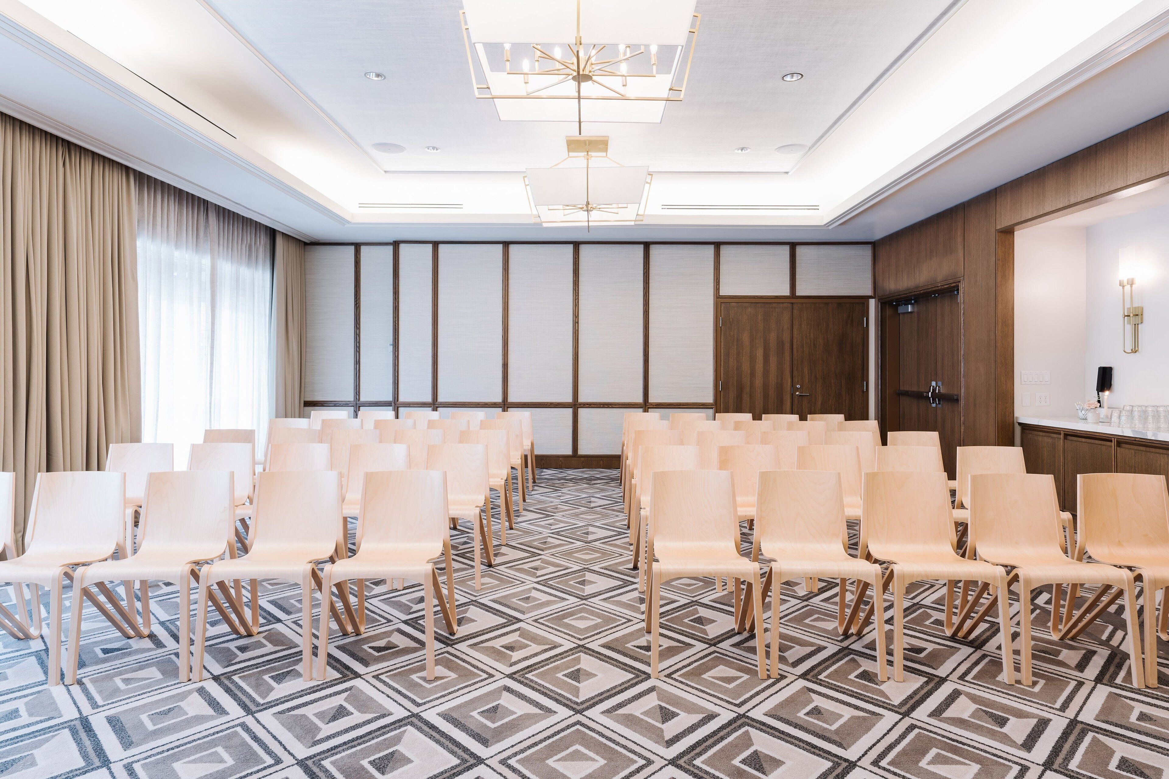 Un salón de conferencias con filas de sillas, una alfombra estampada y una lámpara de araña grande.