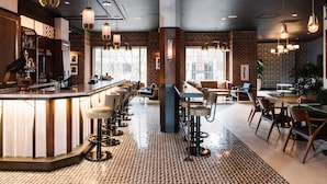 Un área de bar moderna con una barra alargada, taburetes y luces colgantes.