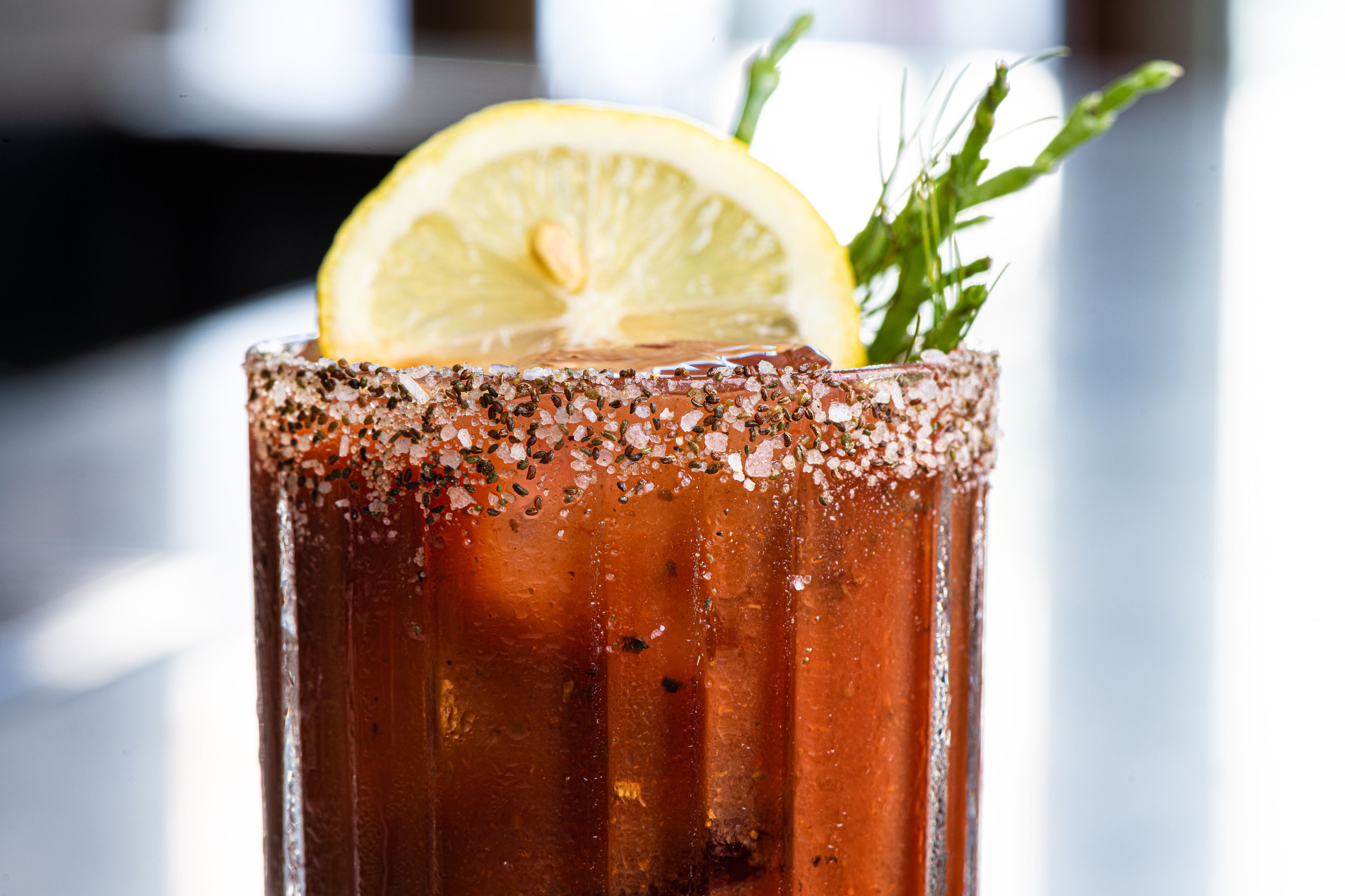 Primer plano de un cóctel Bloody Mary, adornado con una rodaja de limón y hierbas.
