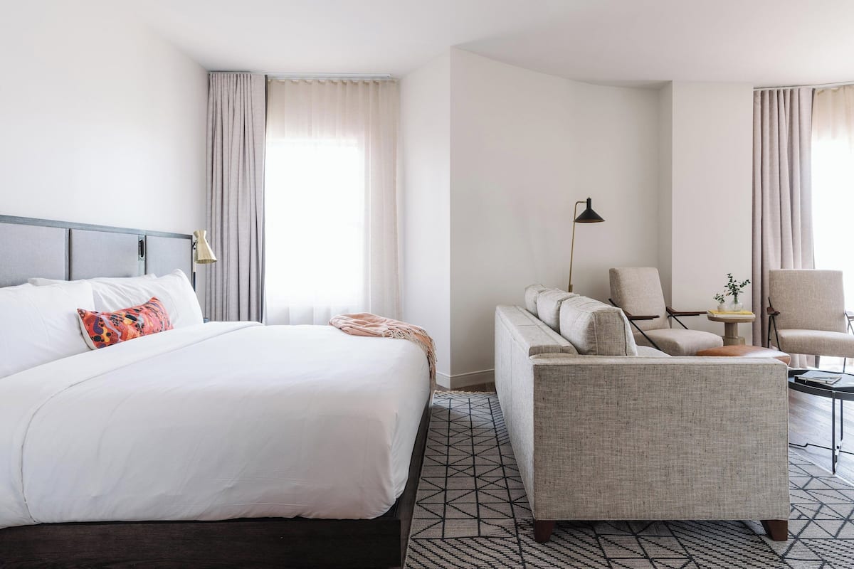 Ein Hotelzimmer mit Bett, Sofa, Sessel, Lampe und kleinem Tisch.