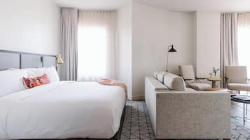 A hotel room with a bed, a sofa, a chair, a lamp, and a small table.