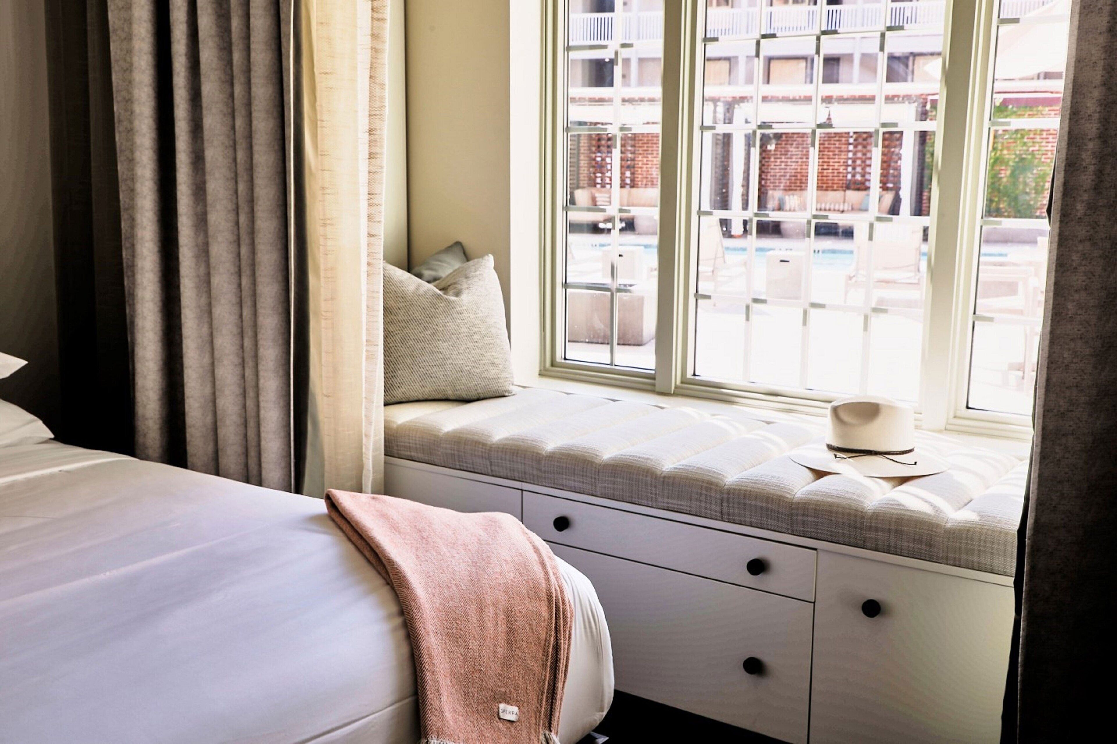 Quarto com cama, um assento à janela com almofadas e vista para o exterior.