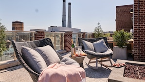 Una terraza en la azotea con sillones de mimbre, una pequeña mesa con una botella y vasos, y una bandeja de aperitivos.