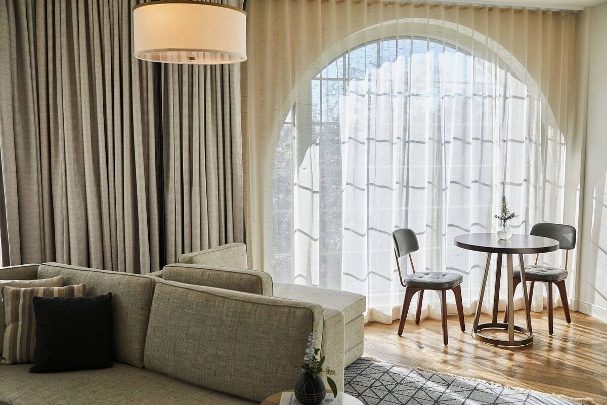 Ein modernes Wohnzimmer mit einer Couch, zwei Sesseln, einem Tisch und einem großen Bogenfenster.