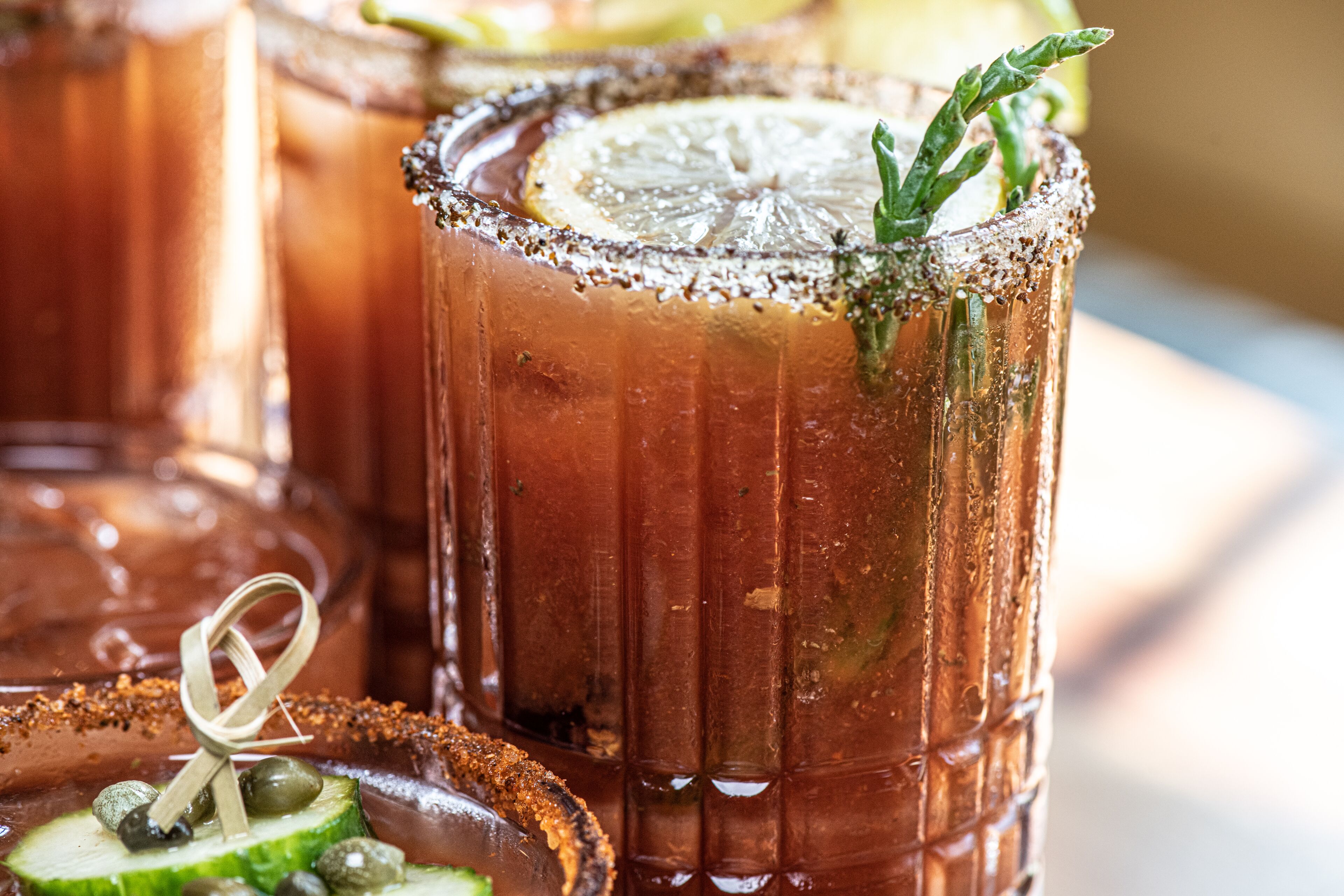A close-up of a cocktail with a salted rim and garnished with a lemon slice and a sprig of rosemary.