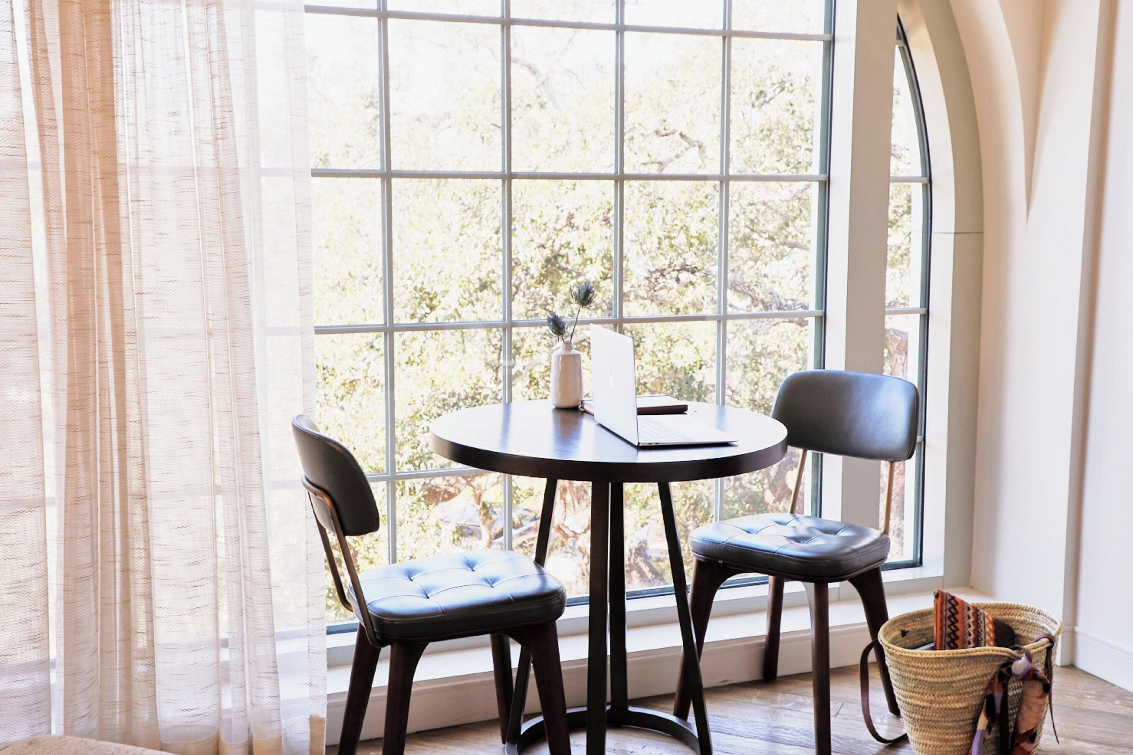 A room with a large window, a round table, two chairs, and a woven basket.