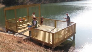 Une terrasse en bois avec une table de pique-nique et des bancs, donnant sur un lac paisible.