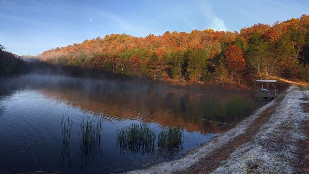 Un lac paisible, avec un quai et un chalet sur la rive, entouré d’arbres aux couleurs automnales.