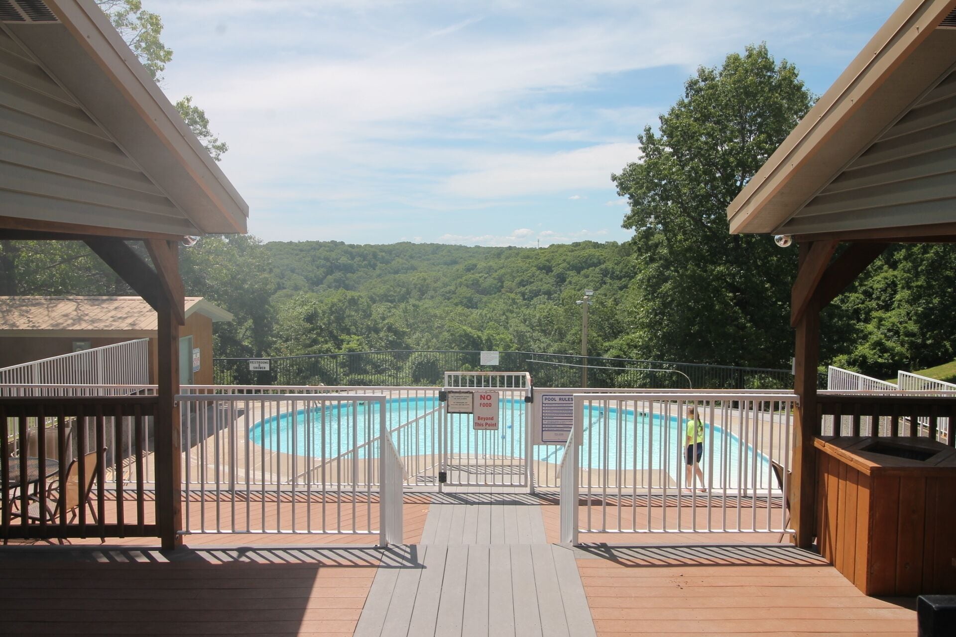 A wooden deck with a pool, surrounded by a metal fence, and a view of a forested area.