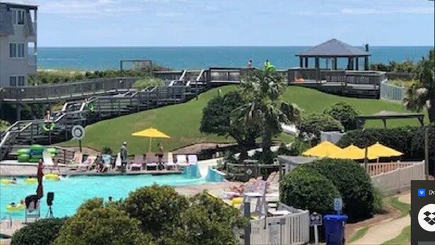 A pool area with a view of the ocean, a gazebo, and a building with a balcony. - 2/2 Ocean View Condo at APATB Resort (Atlantic Beach, NC)