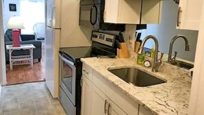 A compact kitchen with white cabinets, a stainless steel sink, and a countertop. - 2/2 Ocean View Condo at APATB Resort (Atlantic Beach, NC)