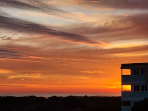 A building with a flat roof and multiple windows, located near a body of water with a sunset in the background.