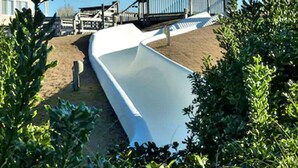 A white slide in a sandy area with a wooden deck and a building in the background. - 2/2 Ocean View Condo at APATB Resort (Atlantic Beach, NC)