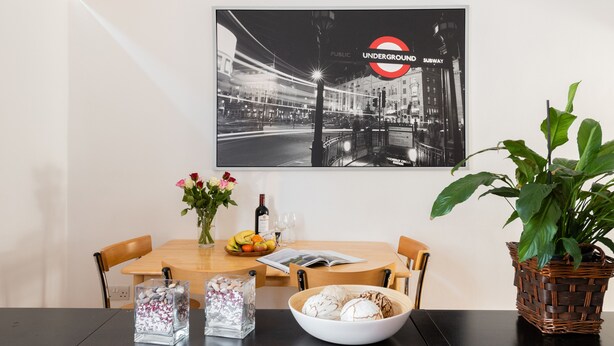 Ein Essbereich mit Tisch, Stühlen, einer Blumenvase, einer Brot-Schale und einem schwarz-weißen Foto einer U-Bahn-Station.