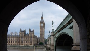 Blick auf die Houses of Parliament und Big Ben durch einen Bogen, mit einer Brücke im Vordergrund.