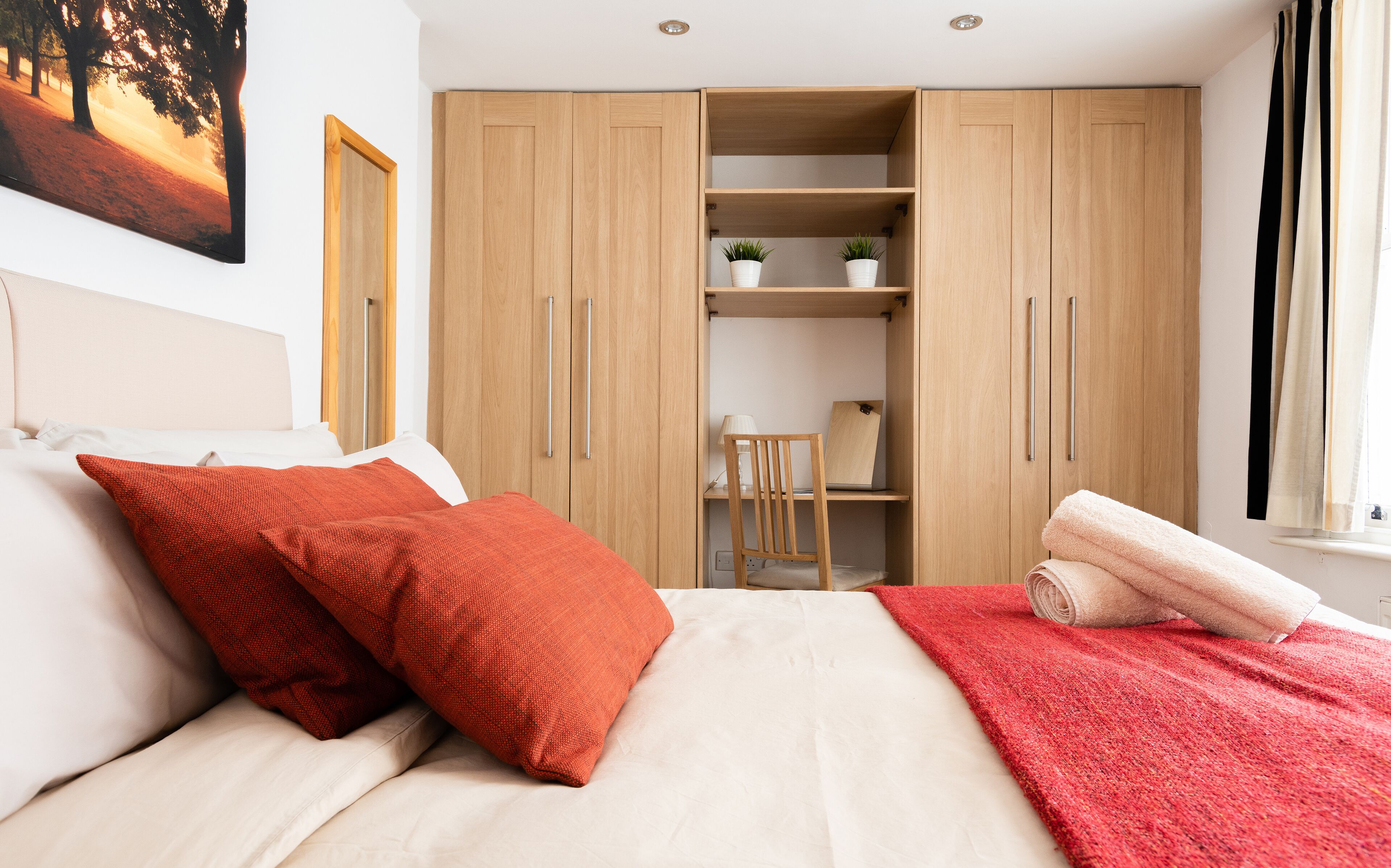 Un dormitorio con una cama, almohadas rojas, una colcha roja, un armario de madera y un escritorio con una silla.