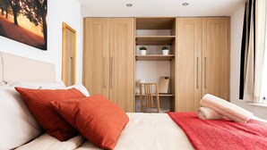 Ein Schlafzimmer mit einem Bett, roten Kissen, einer roten Decke, einem Holzschrank und einem Schreibtisch mit Stuhl.