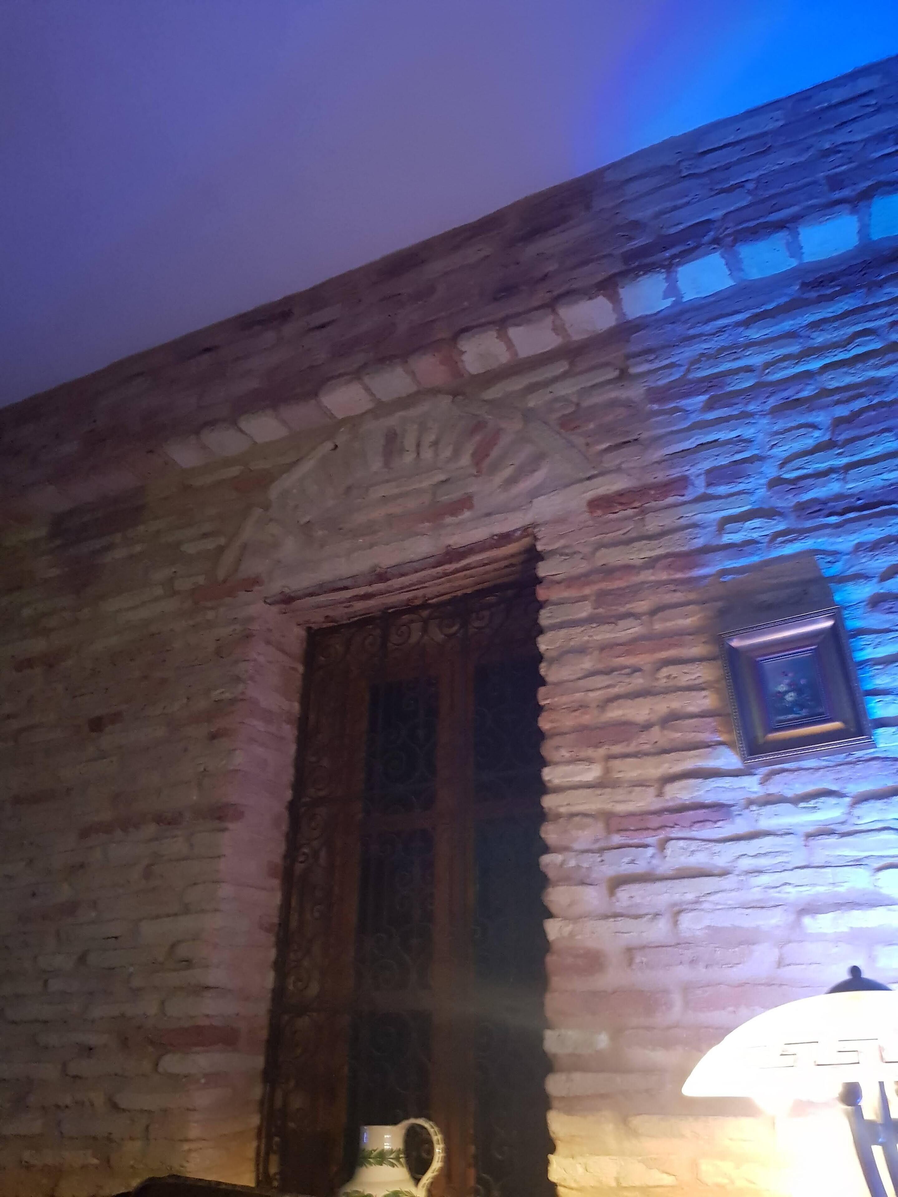 A room with a stone wall, a wooden door with intricate carvings, and a small framed picture on the wall.