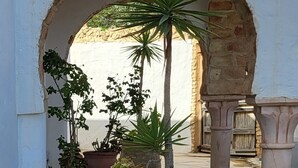 An outdoor courtyard with stone flooring, potted plants, and a white wall with an archway. - Luxury Home With Unique Gulf View Of Hammamet (Hammamet)
