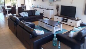A modern living room with a sofa set, a coffee table, a TV, and a dining area with chairs and a table.
